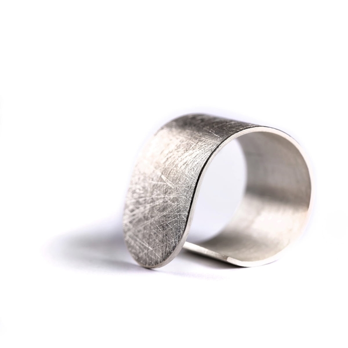 Duży, srebrny, asymetryczny i minimalistyczny pierścionek z kolekcji Halfring z mocno wyszczotkowaną matową powierzchnią, i błyszczącymi krawędziami i bokami dla kontrastu. Zaprojektowany w pracowni Saffa w Katowicach.