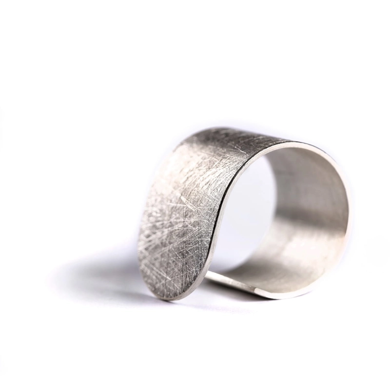 Duży, srebrny, asymetryczny i minimalistyczny pierścionek z kolekcji Halfring z mocno wyszczotkowaną matową powierzchnią, i błyszczącymi krawędziami i bokami dla kontrastu. Zaprojektowany w pracowni Saffa w Katowicach.