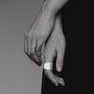 Luźno puszczone dłonie,na czarnym tle, na 2 palcach srebrne pierścionki z najnowszej kolekcji Halfring, wykonane ręcznie w trudnej do znalezienia pracowni projektowania biżuterii Saffa w Katowicach. Lśniąca, duża, otwarta, unikatowa biżuteria.