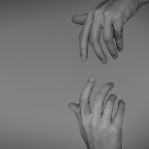 Dłonie spoglądające na siebie w pionie. Na jednym palcu srebrny pierścionek z najnowszej kolekcji Halfring, duży, otwarty, z szeroką obrączką, wyszczotkowany na powierzchni i wypolerowany na krawędziach. Minimalistyczny w stylu marki Saffa.