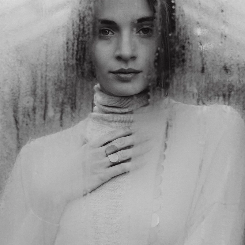 Zmysłowa kobieta en face, w jasnym golfie, w srebrnej biżuterii z tej samej kolekcji Halfring, w kolczykach, naszyjniku z połówek i w dwóch pierścionkach, symetrycznym i asymetrycznym. Satynowe i wybłyszczone, dobrym stylu marki Saffa.