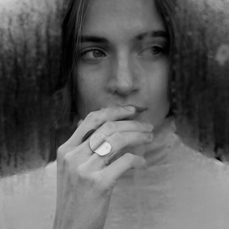 Zmysłowa kobieta en face, zza zaparowanego okna, z dłonią przy ustach, w dwóch srebrnych pierścionkach, otwartych, wyszczotkowanych na powierzchni, w unikatowym stylu marki Saffa ze Śląska, z pracowni, którą trudno znaleźć w Katowicach.