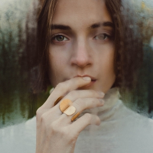 Dwa złocone, duże, otwarte pierścionki, na palcach pięknej zamyślonej kobiety, z dłonią przy ustach, wybłyszczone na rantach, lśniące,wykonane ręcznie w pracowni projektowania biżuterii na Śląsku, w trudnejj do znalezienia pracowni ;).