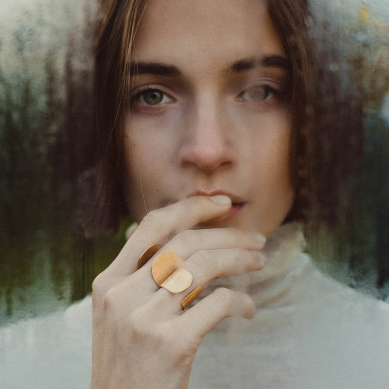 Dwa złocone, duże, otwarte pierścionki, na palcach pięknej zamyślonej kobiety, z dłonią przy ustach, wybłyszczone na rantach, lśniące,wykonane ręcznie w pracowni projektowania biżuterii na Śląsku, w trudnejj do znalezienia pracowni ;).