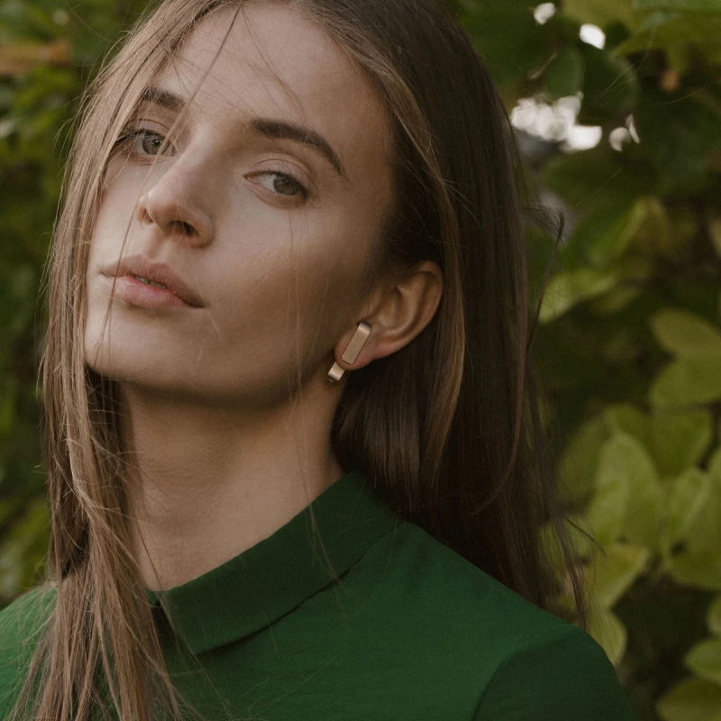 piękna kobieta w zieleni w złotych lokczykach minimalistycznych z rozwianymi włosami. ponadczasowy desing, prektowanie wyjątkowe, design jewelry from poland